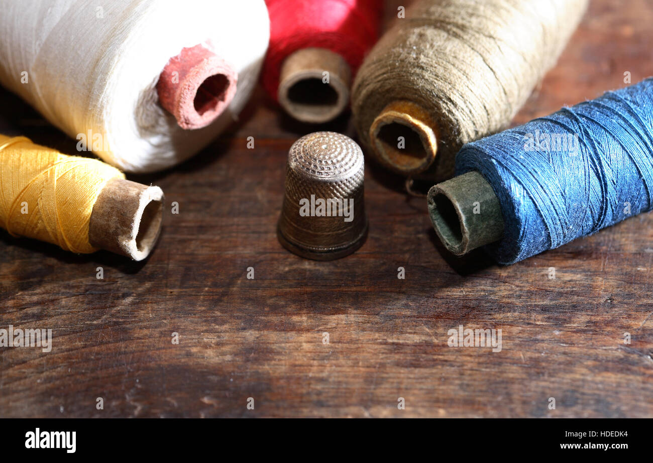 Thimble near spools of color threads on old wooden background Stock Photo