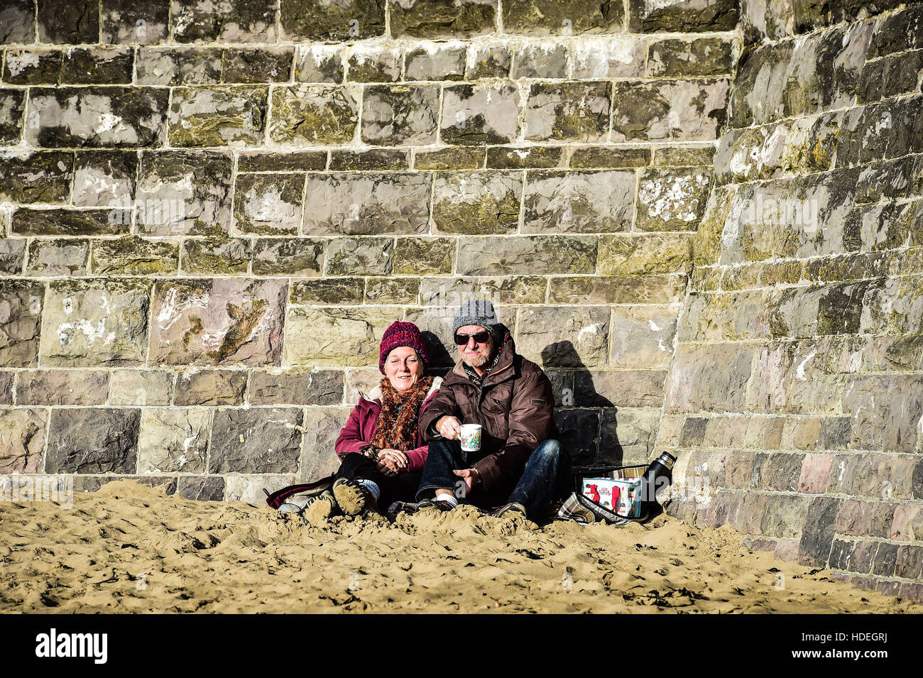 People relax with a flask of tea on the beach at Barry Island, Vale of Glamorgan, Wales, where clear skies and bright sunshine dominate the South Wales coastline as December temperatures continue to be mild. Stock Photo
