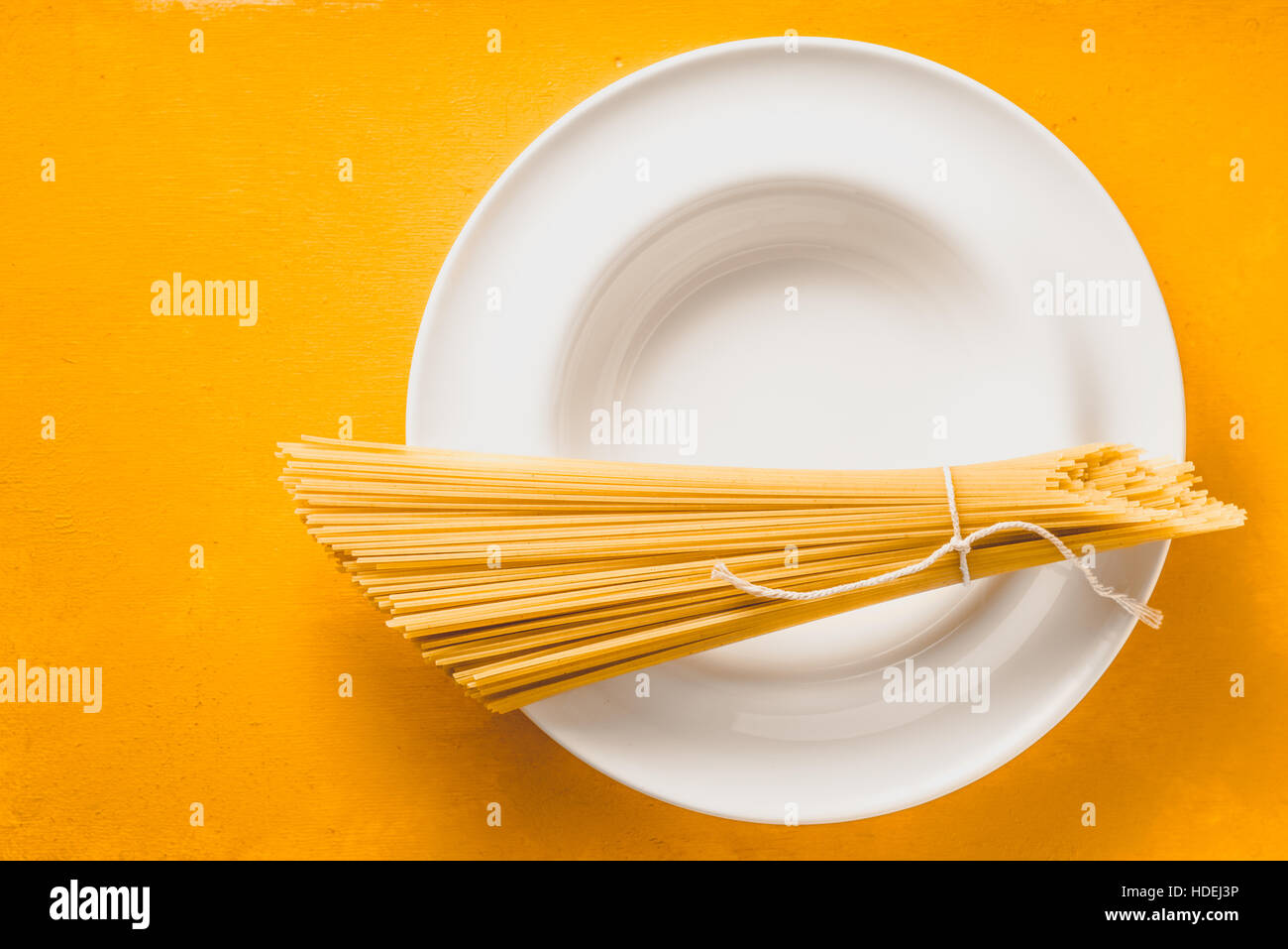 Bunch of raw spaghetti  on the white plate on the yellow background top view Stock Photo