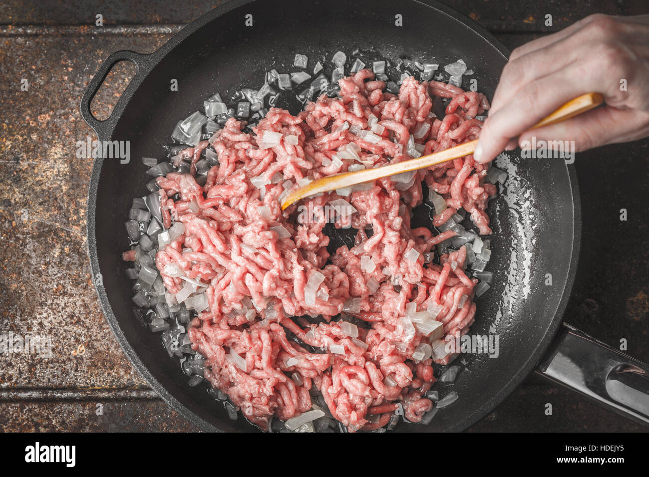 Raw minced meat with sliced onion in the pan with wooden spoon in the hand Stock Photo