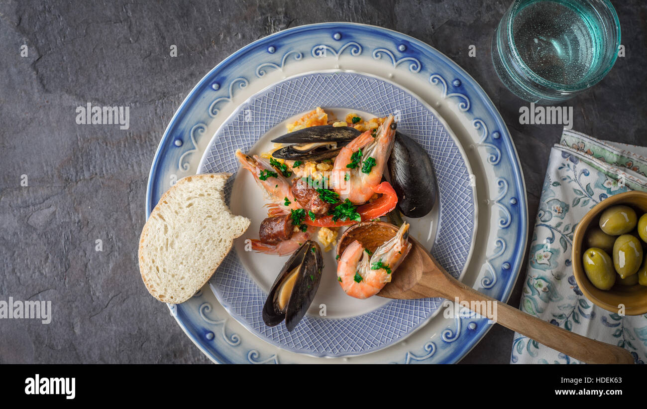 Plate with paella on the dark stone table with different accessories top view Stock Photo