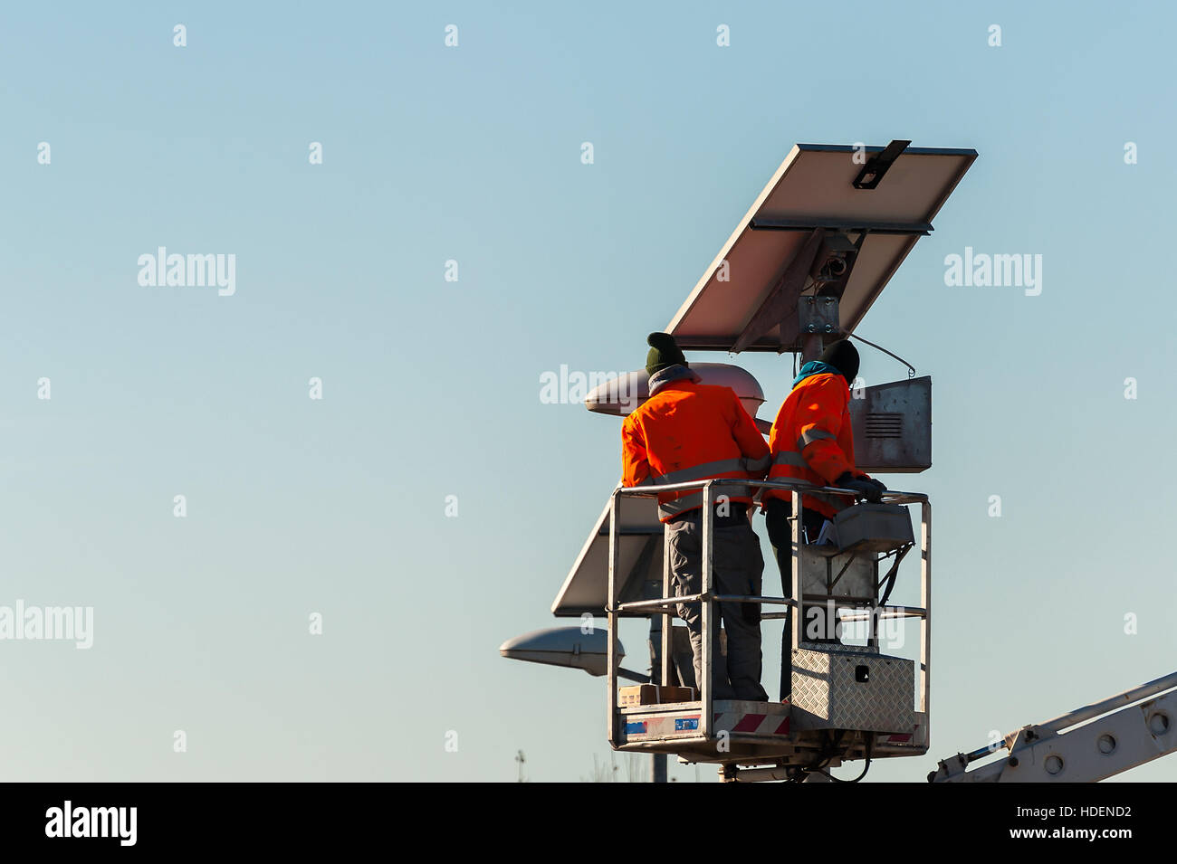 Workers in lift bucket during the maintenance of streetlight powered by a solar panel. Stock Photo