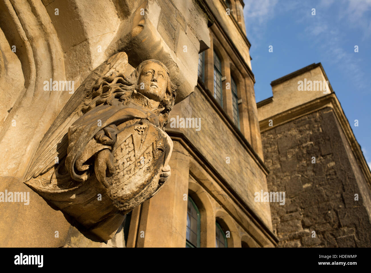 Medieval Gothic sculpture representing an angel with long hair holding a shield engraved on brown stone on the exterior of an ancient building Stock Photo