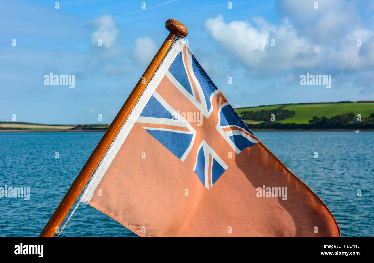 Red Ensign in summer morning sun in front of azure rippled sea and green fields. Stock Photo