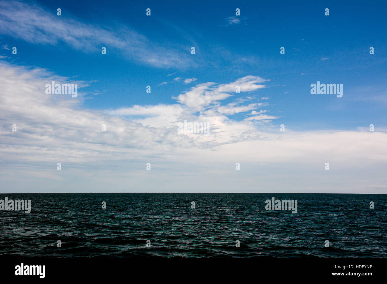 Patterned white clouds in a blue sky over a rippled azure sea. Stock Photo