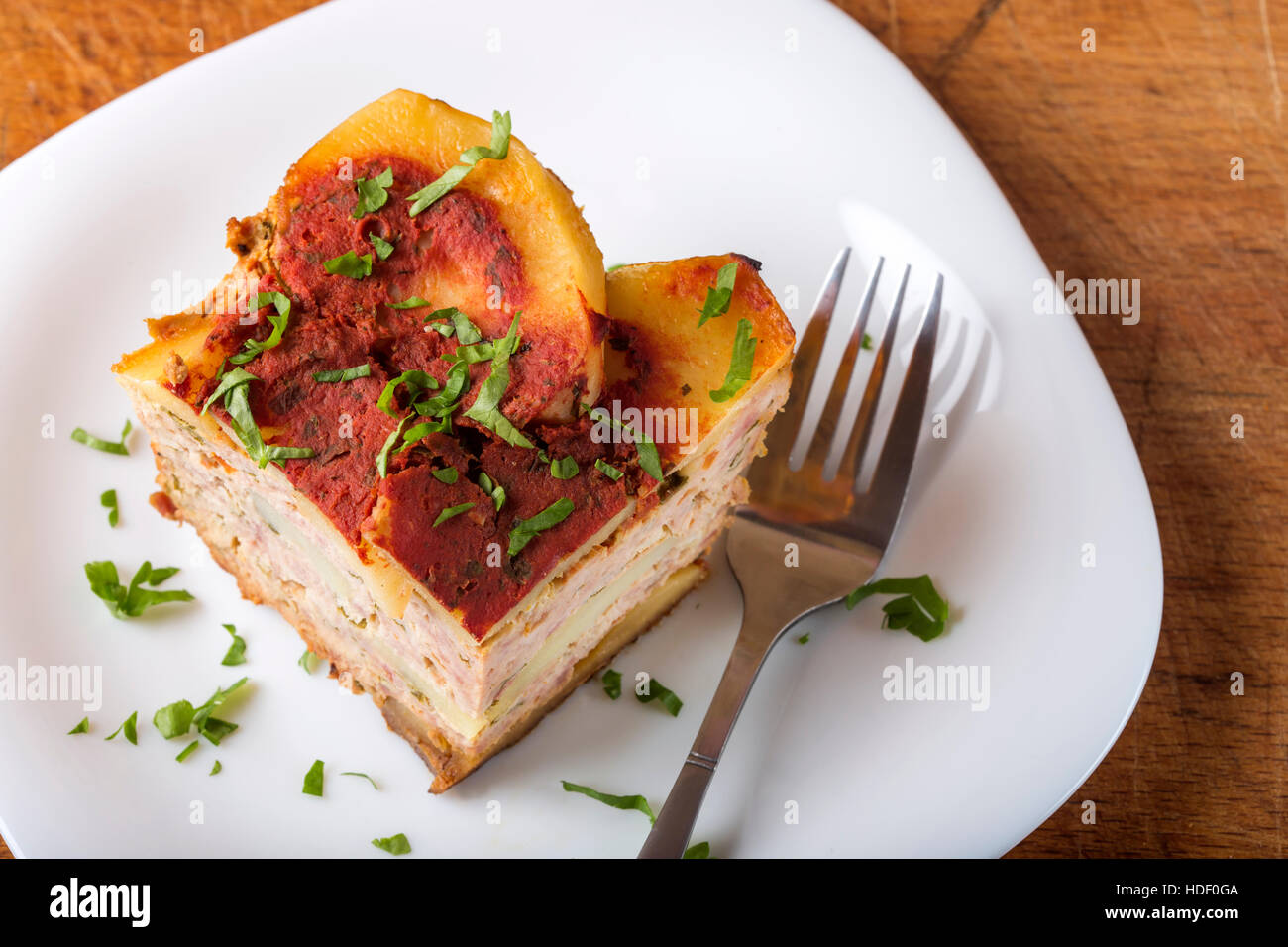 Portion of delicious layered moussaka made with meat and potatoes, on plate with fork and parsley Stock Photo