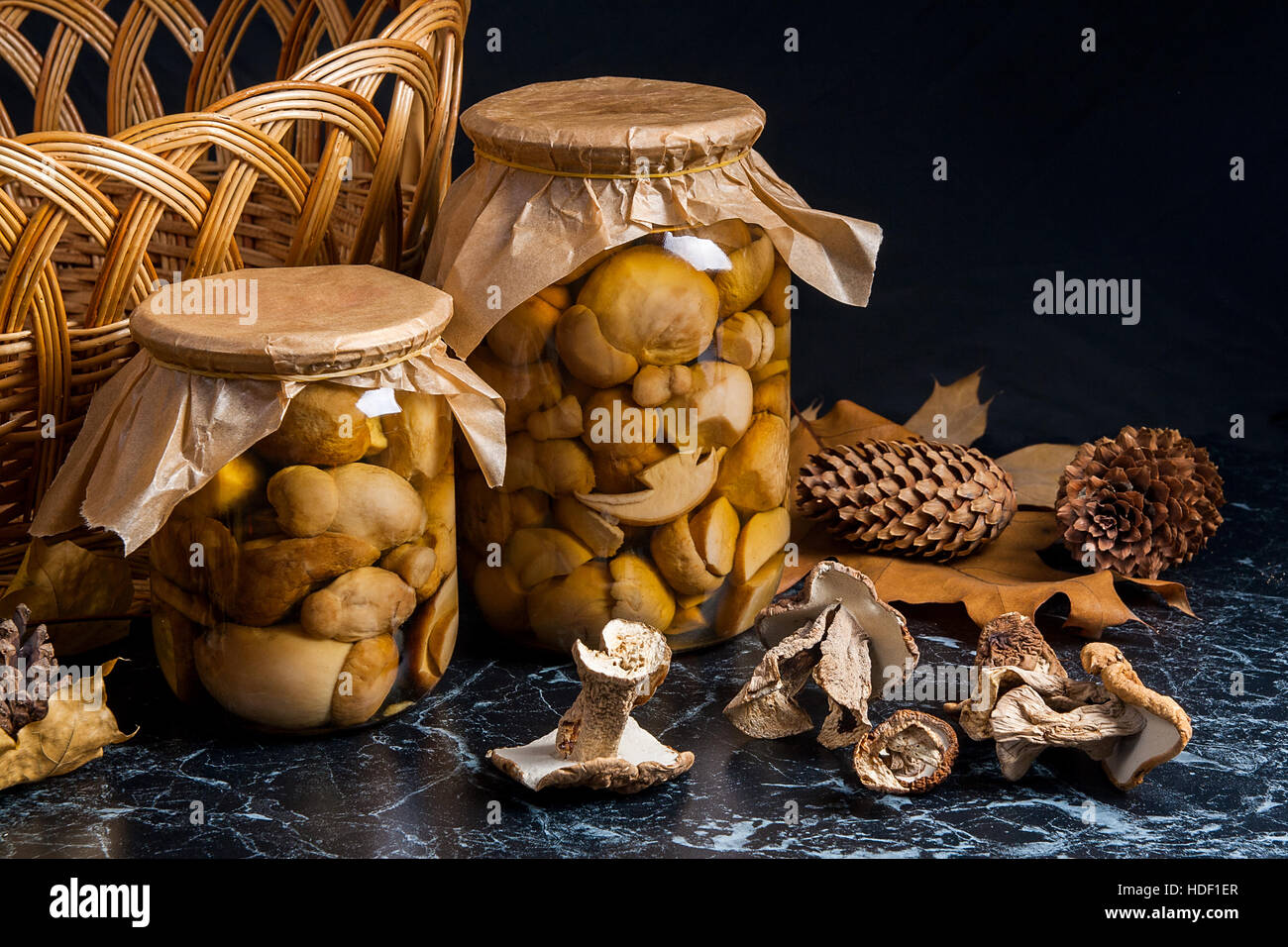 Two glass jars with wild marinated mushrooms on black marble background