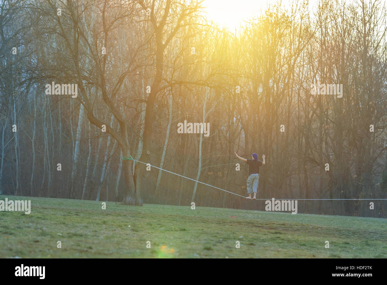 Handsome young man walking on slackline in the park at sunset Stock Photo