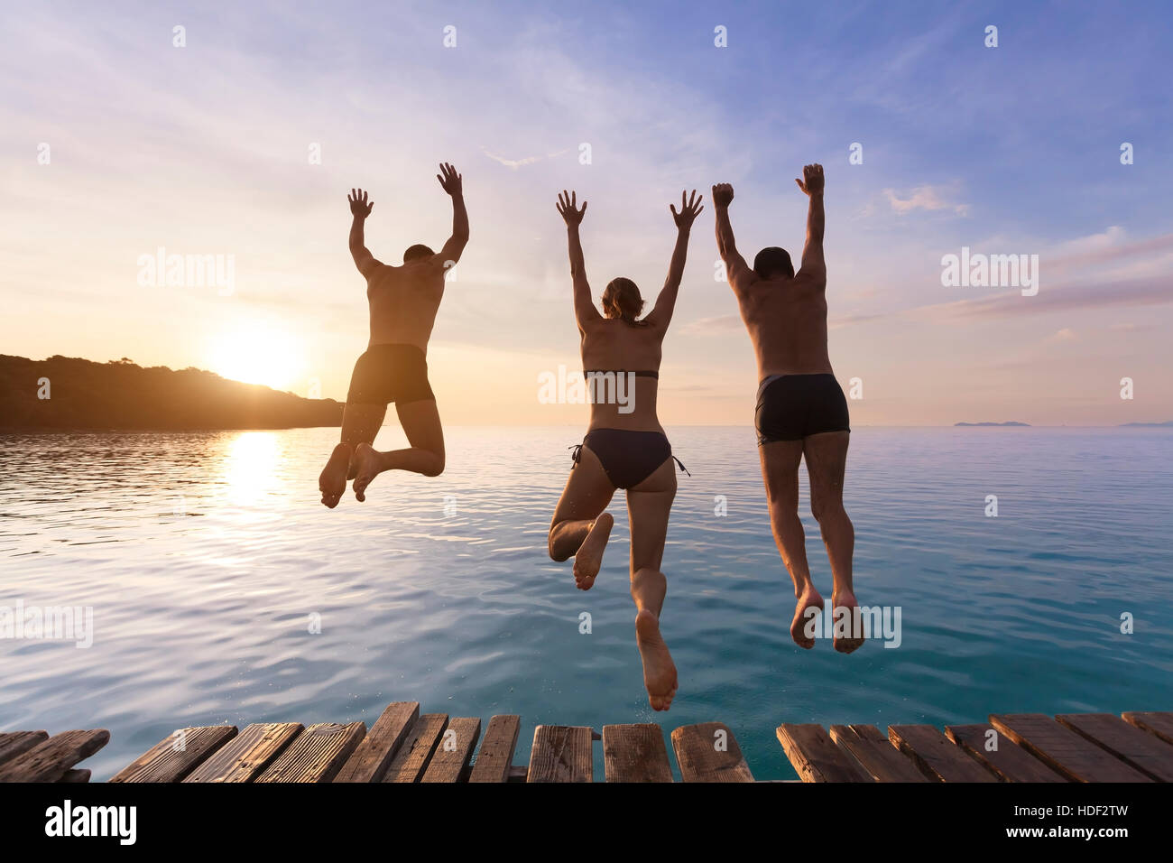 Group of happy people having fun jumping in the sea water from a pier Stock Photo