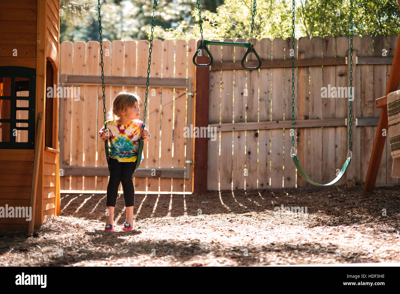 Girl on swing. front view. girl looking away. fence on background Stock Photo