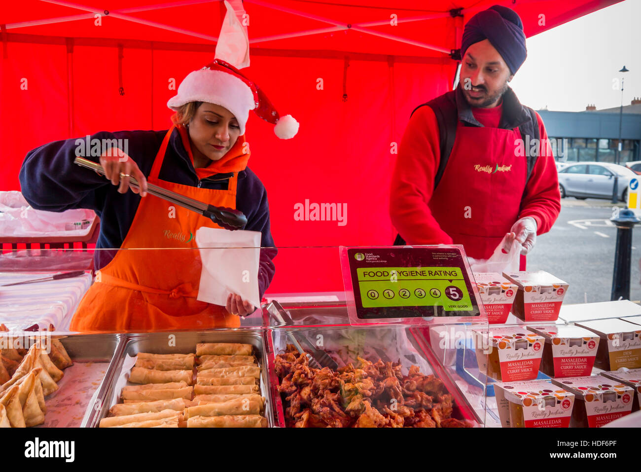 A man and woman Sikh  stall holders at a UK Christmas farmer's market serving Curry Sauces and cooked 'Really Indian' food Stock Photo