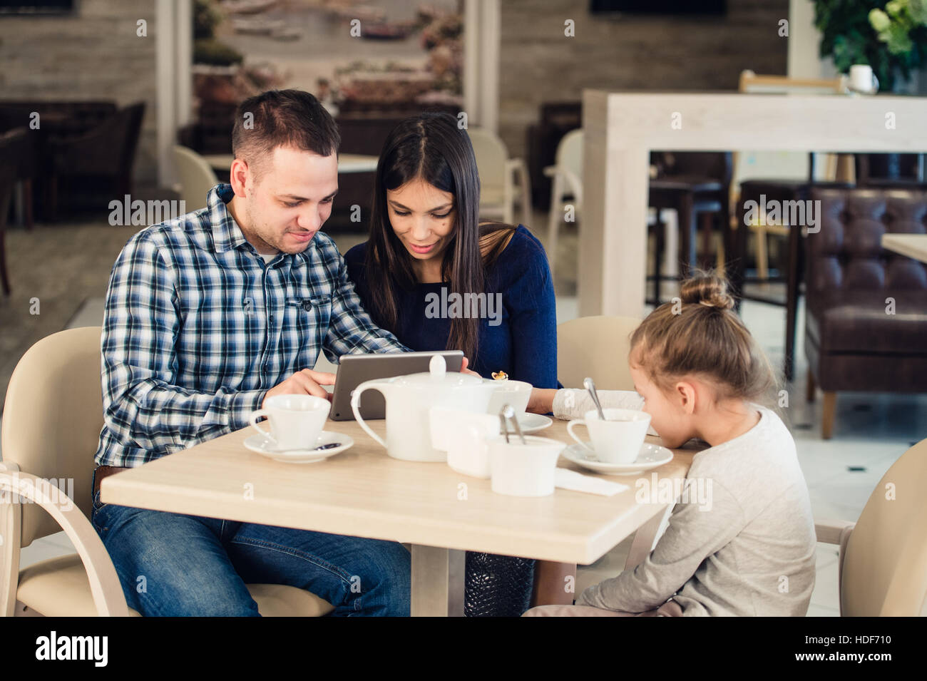 Family with child in cafe. Mother and father watching on tablet pc while girl waiting Stock Photo