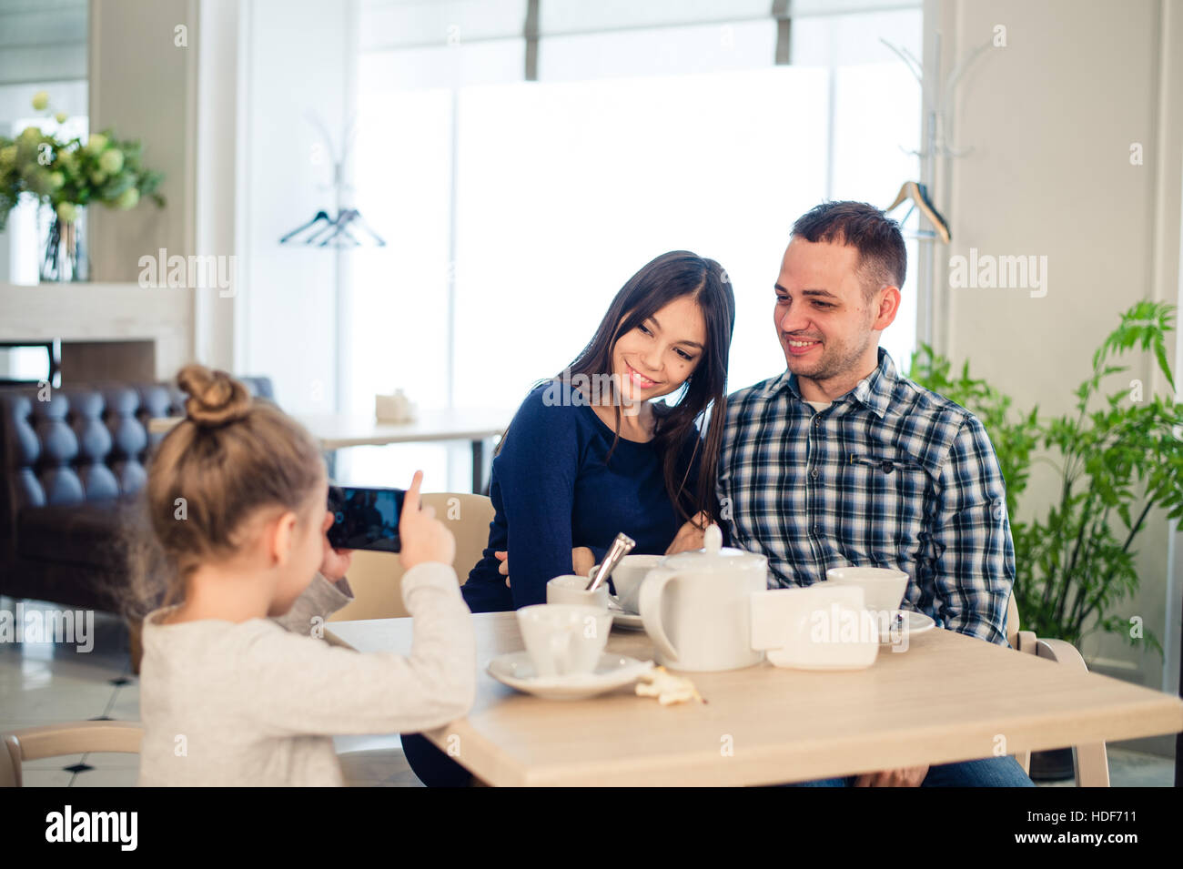 family, parenthood, technology people concept - close up of happy mother, father and little girl having dinner, kid taking photo by smartphone at restaurant Stock Photo