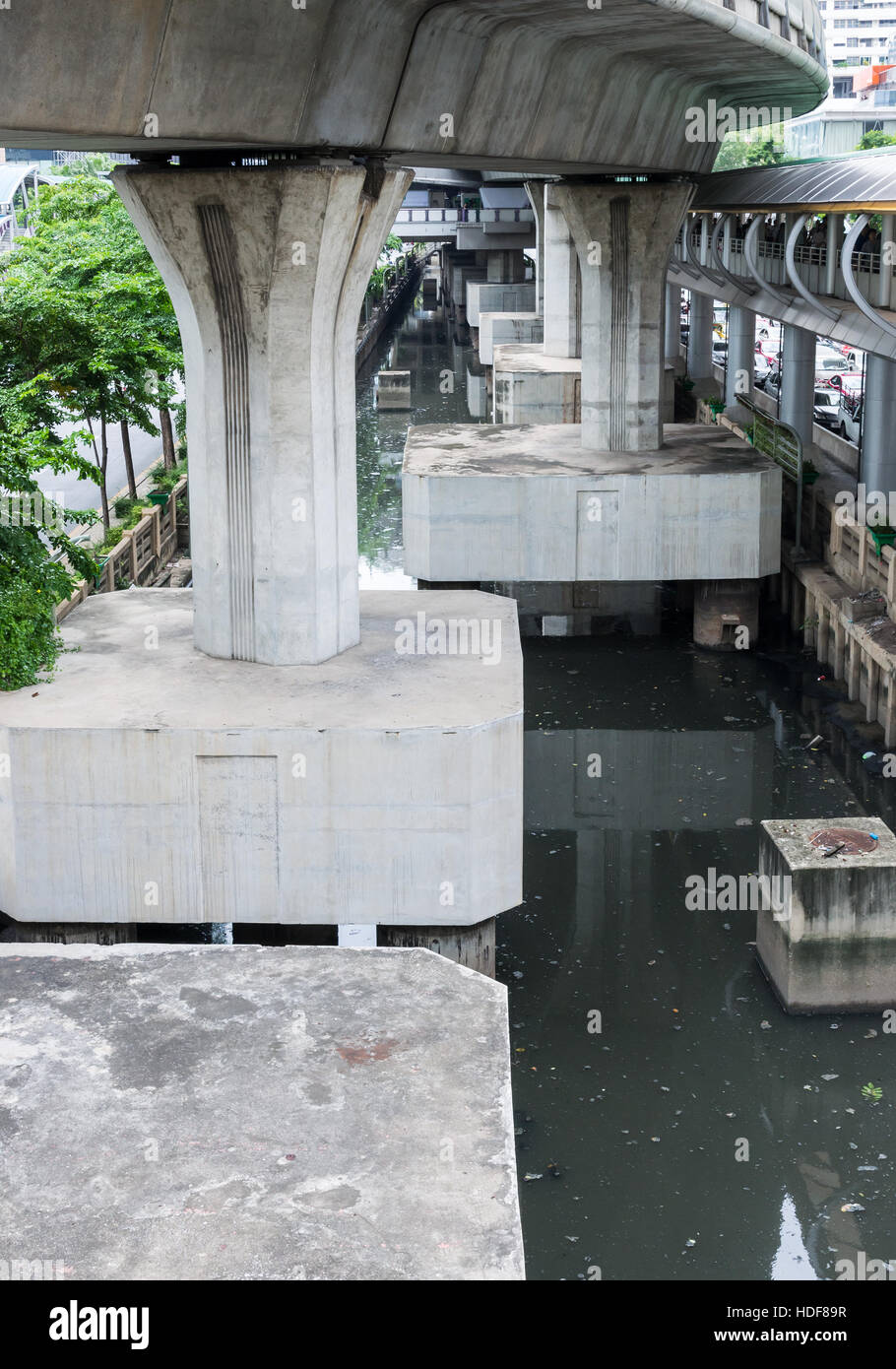 Large concrete pillar of the modern sky train in the dirty canal of the Bangkok, Thailand. Stock Photo