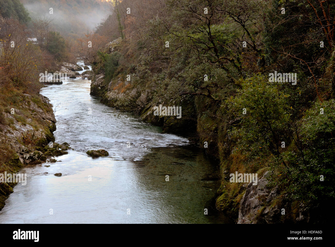 Image of the river in its bed, with fog in the background, which begins to cover the mountains Stock Photo