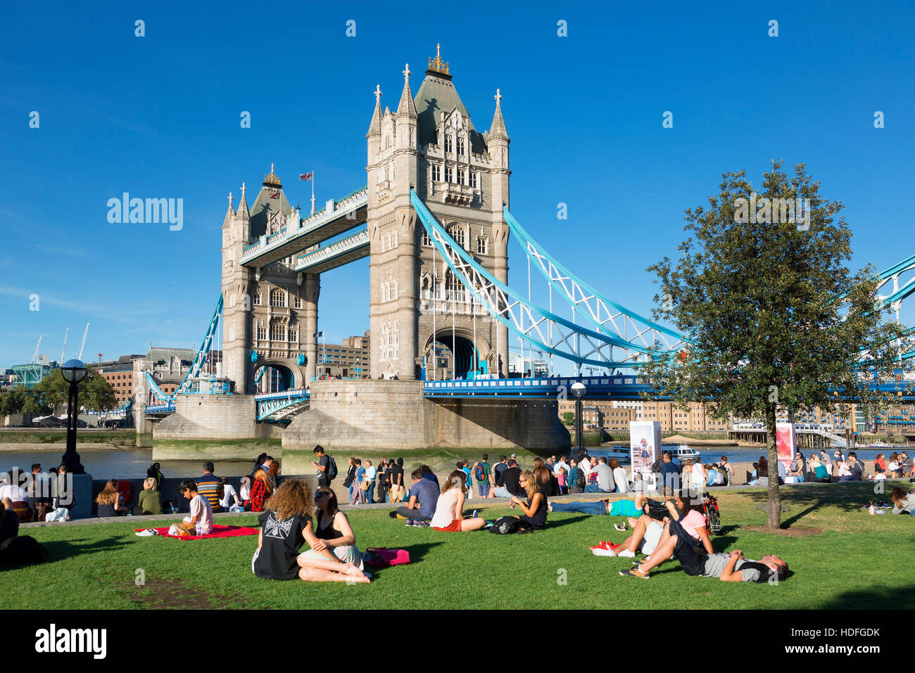 LONDON, The Queen's South Bank Walk London. Tourists enjoy sun and shade by Tower Bridge on the Southbank of the Thames Stock Photo