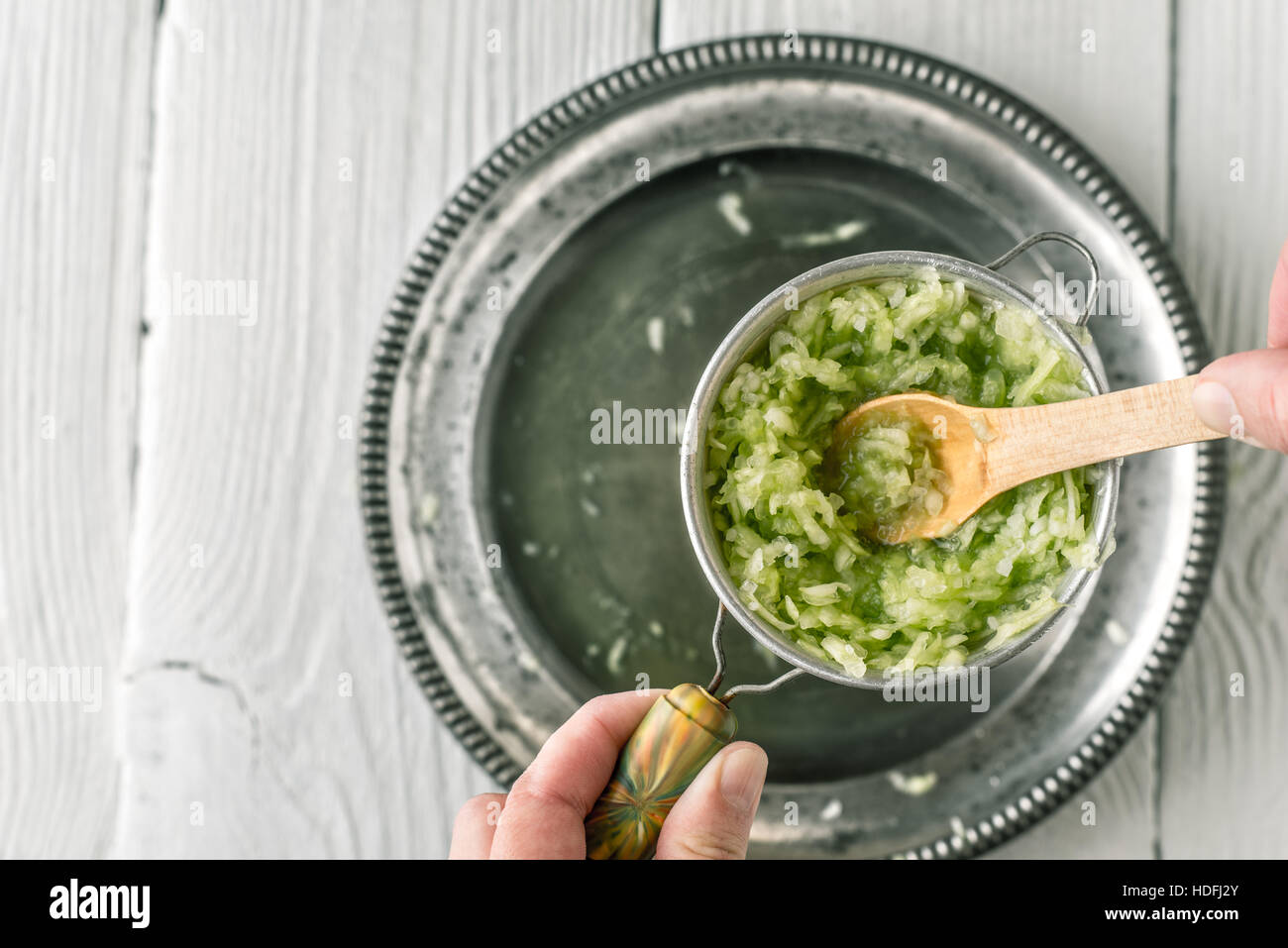 Grated cucumbers in the strainer with wooden spoon top view Stock Photo