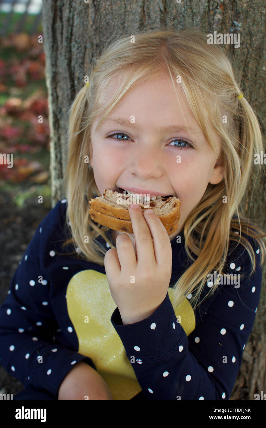 adorable school age girl eating peanut butter and jelly sandwich Stock
