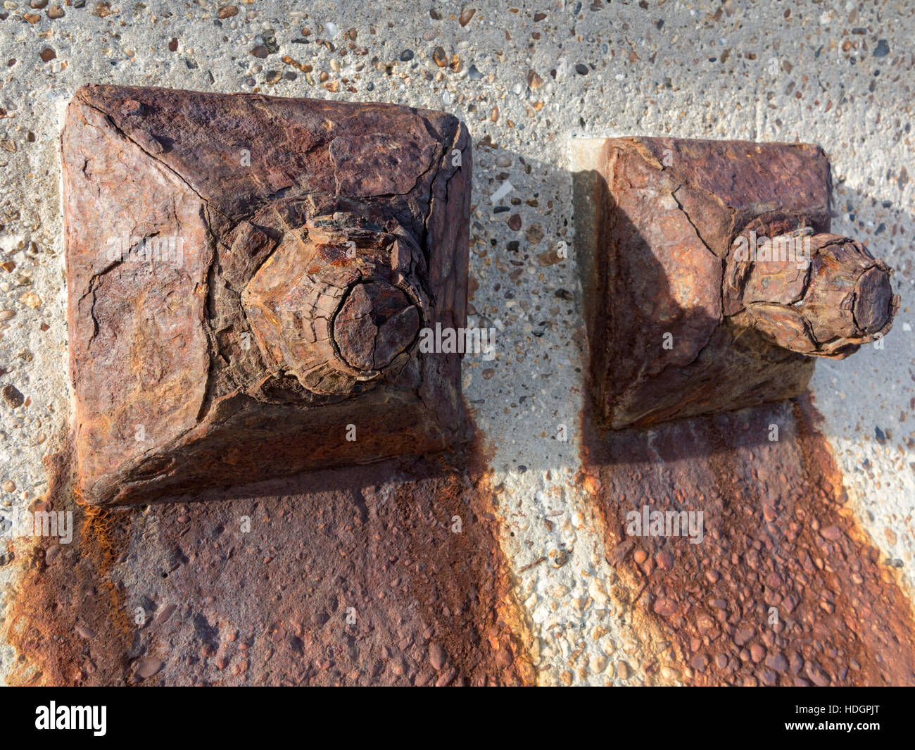 Heavily rust corroded large bolts in a concrete sea wall with oxidation stains running down Stock Photo