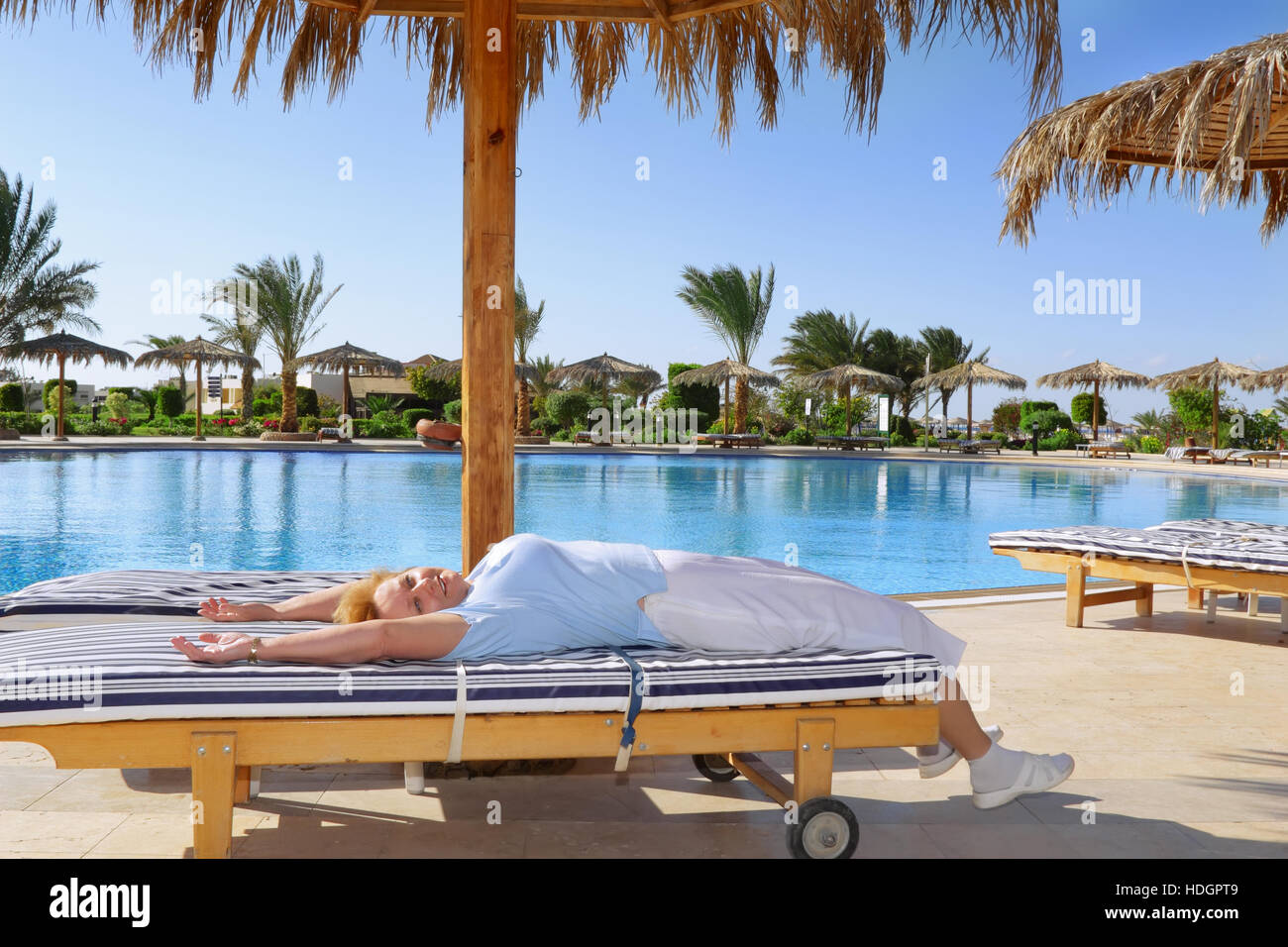 Senior woman lie on chaise longue , near water pool in resortspa hotel