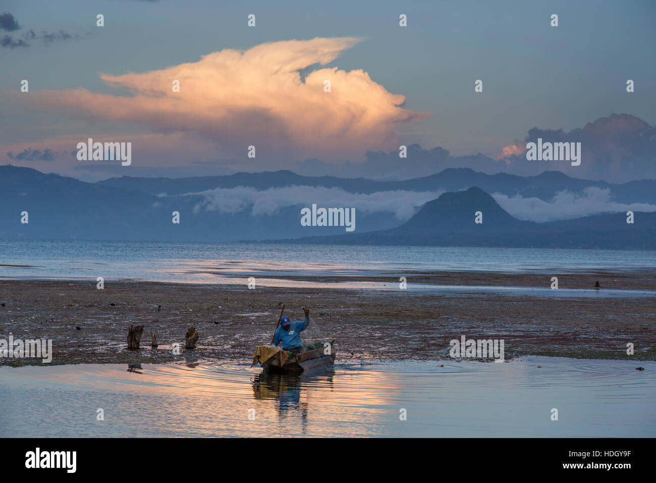 A fisherman pulls in his net into his cayuco at sunset on Lake Atitlan, Guatemala.  In the background is Cerro del Oro and the east shore of the lake Stock Photo