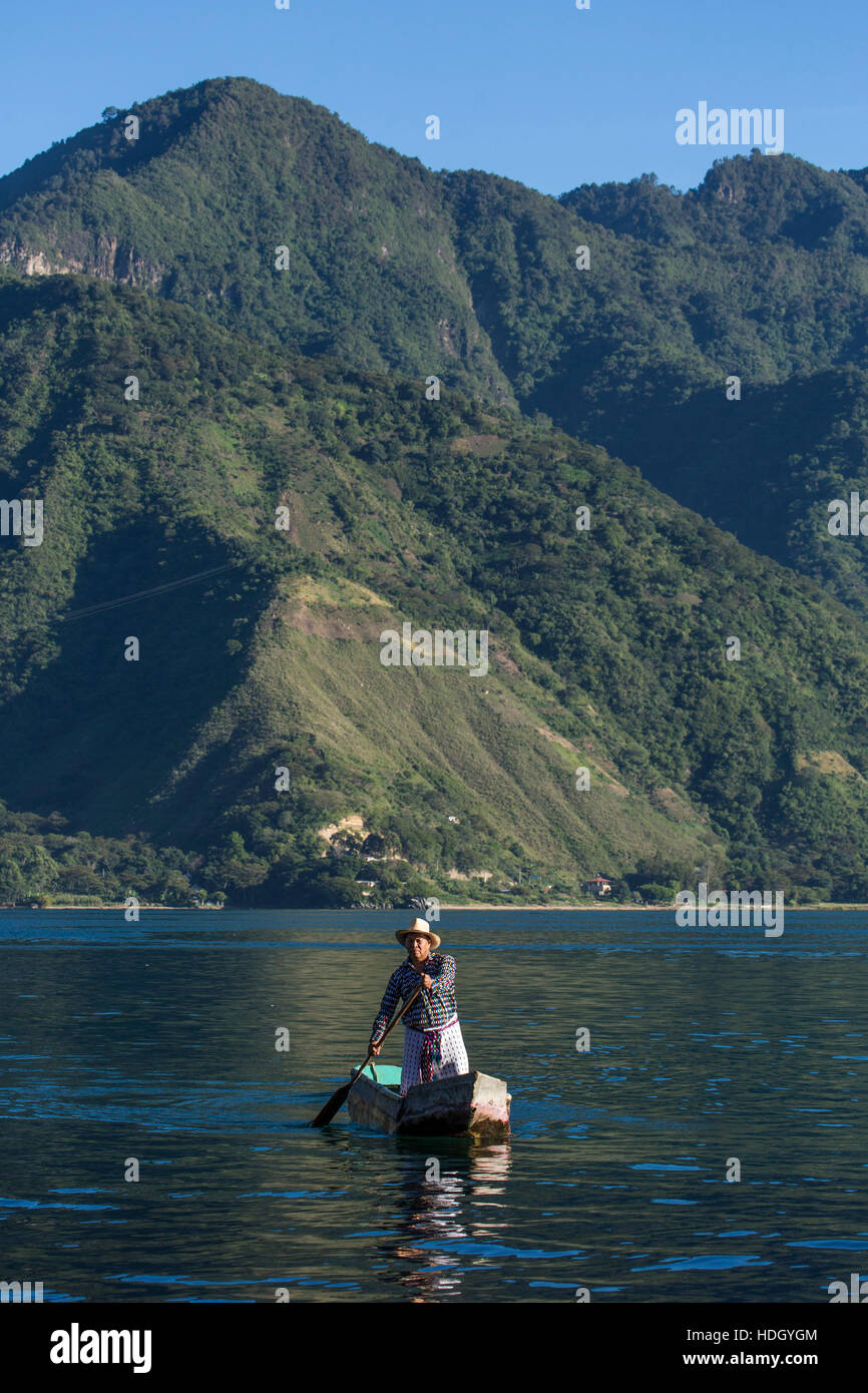 Mayan man in the traditional dress of San Pedro la Laguna paddles a cayuco in early morning light on Lake Atitlan, Guatemala.  Standing.  Steep forest Stock Photo
