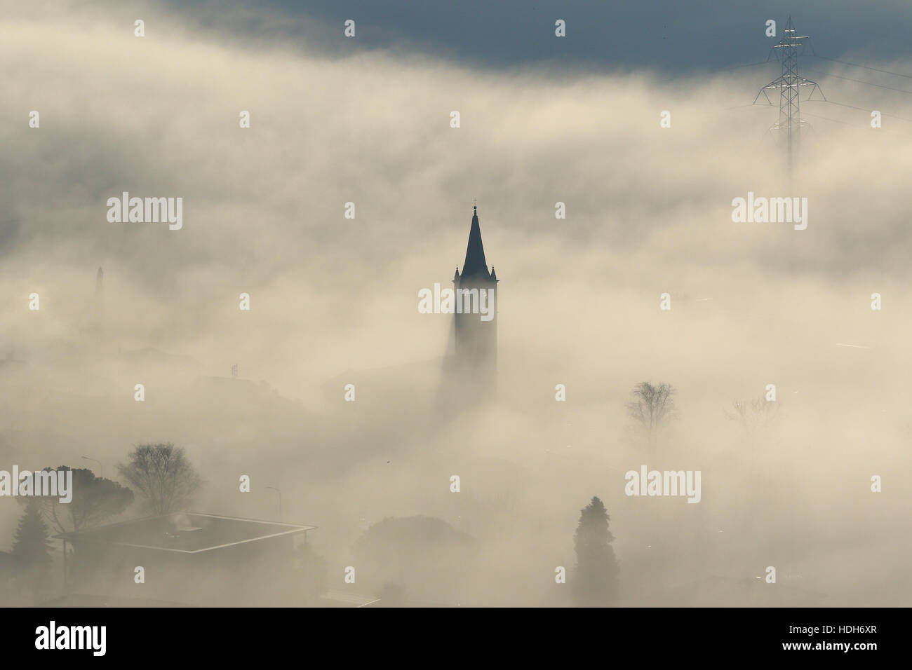 Aerial view of power lines, pylons and church steeple peeking out of winter fog Stock Photo