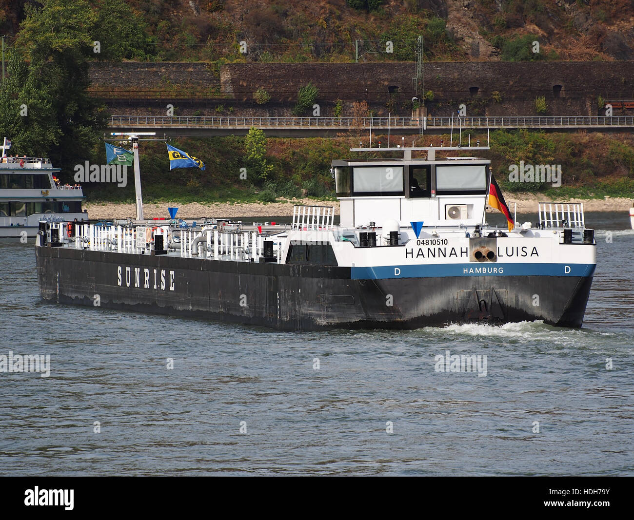 The ship Hanna-Luisa, registered under ENI 04810510, is pictured navigating the Rhine River near Oberwesel in Germany. This image highlights the scenic river landscape and modern maritime vessels. Stock Photo