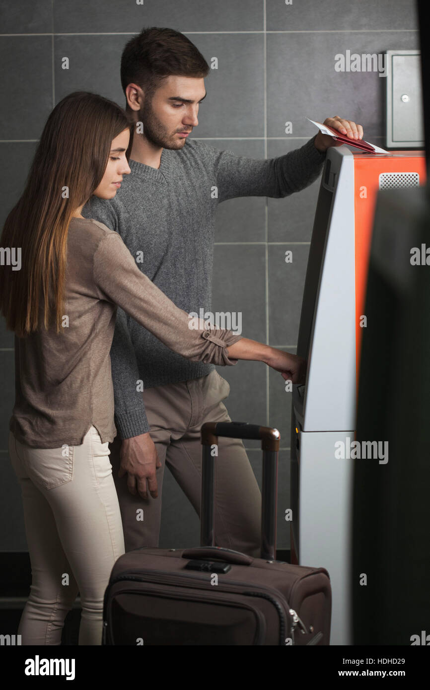 Young couple using ATM machine at airport Stock Photo
