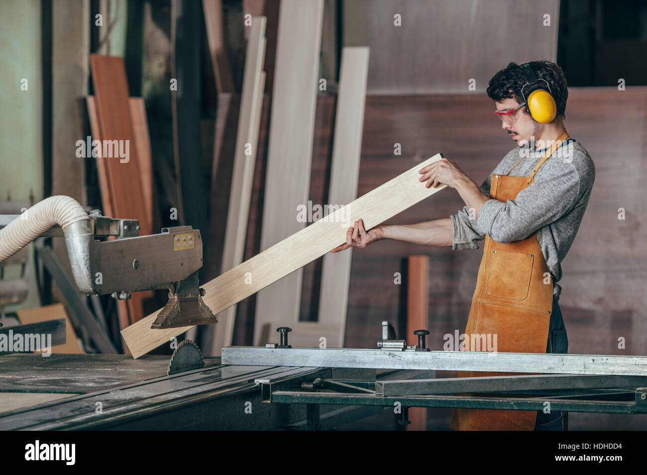 Carpenter examining plank of wood by table saw at workshop Stock Photo