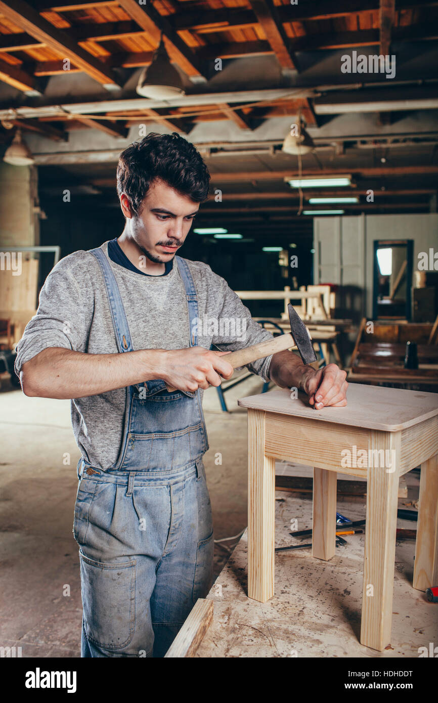 Carpenter hammering nail into wooden stool at workshop Stock Photo