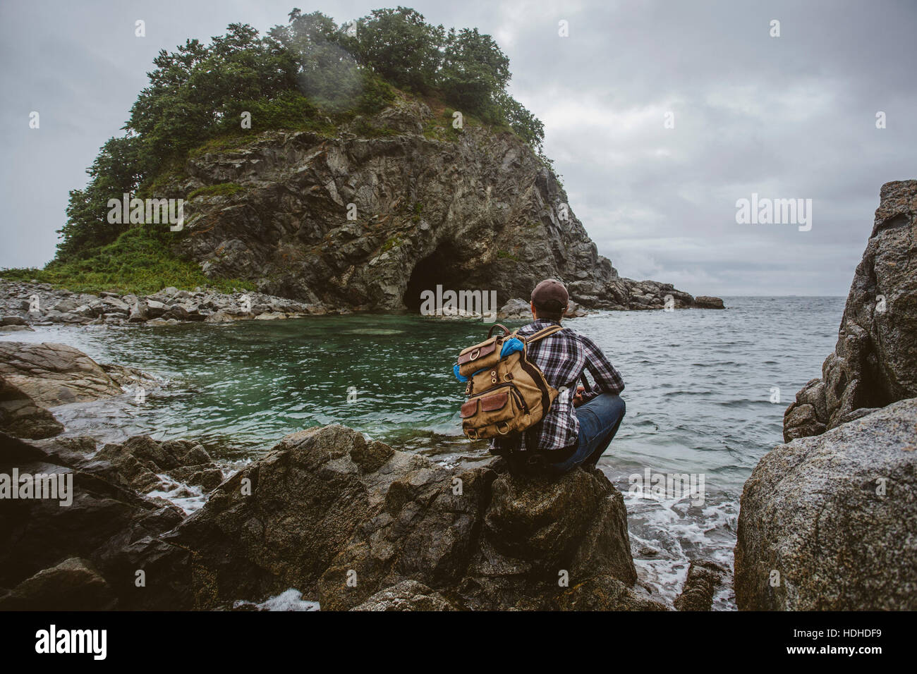 Rear view of hiker sitting on rock formation at beach against sky Stock Photo