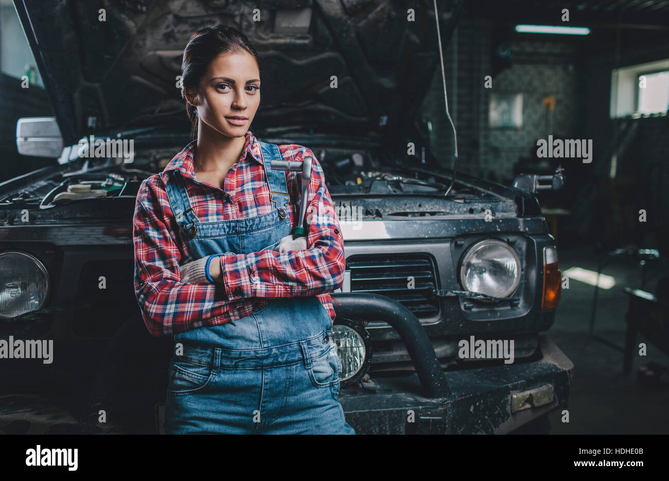 Portrait of confident female mechanic with arms crossed leaning on car at workshop Stock Photo