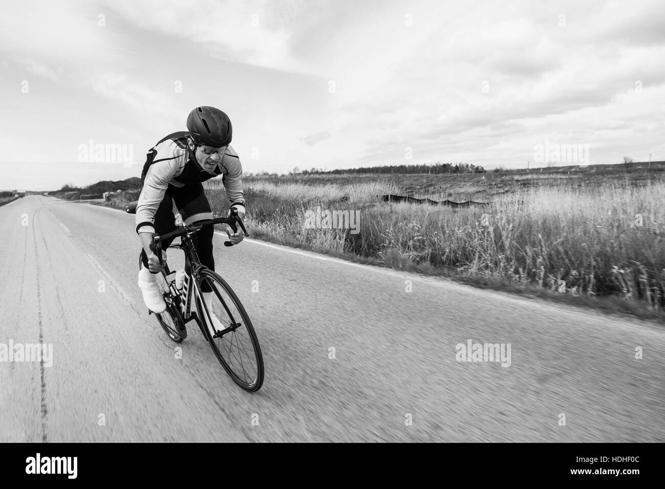 Blurred motion of cyclist riding bicycle on country road by field against sky Stock Photo