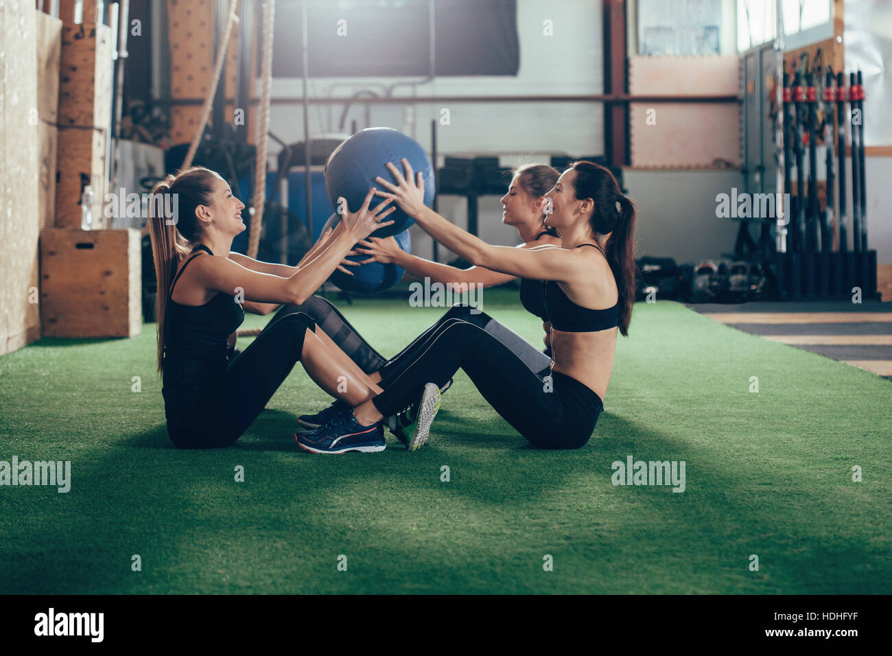 Side view of female athletes exercising with fitness ball while sitting on carpet at gym Stock Photo