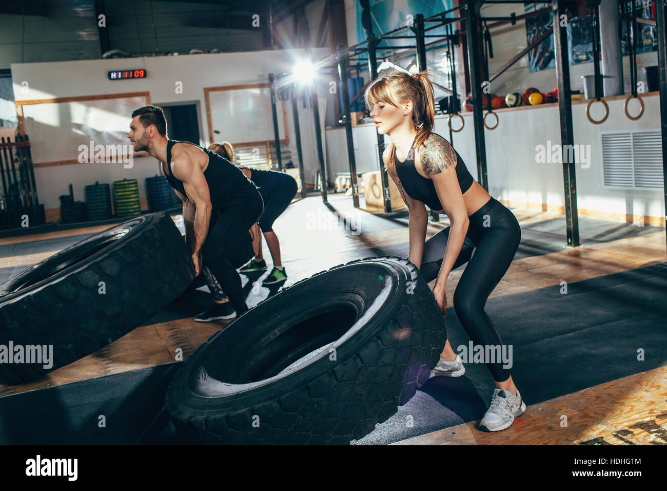 Determined male and female athletes flipping tire at health club Stock Photo