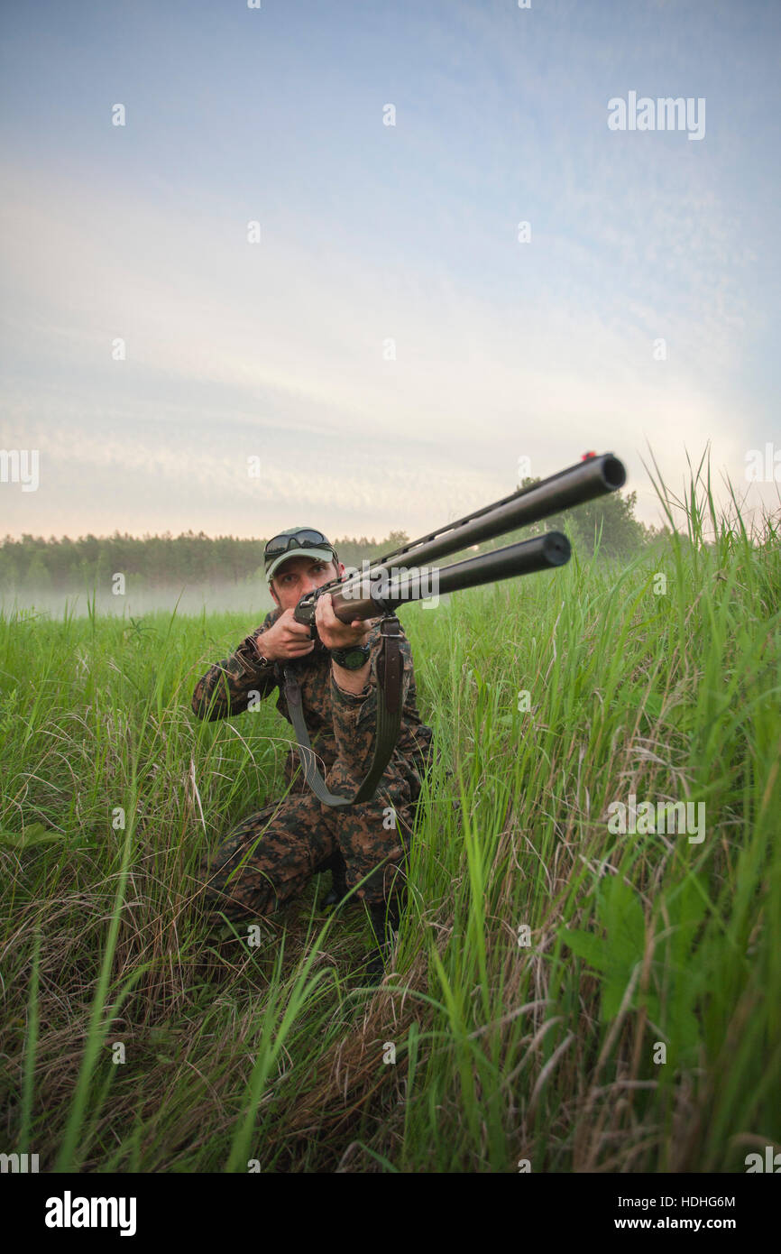 Hunter aiming rifle on field against sky Stock Photo