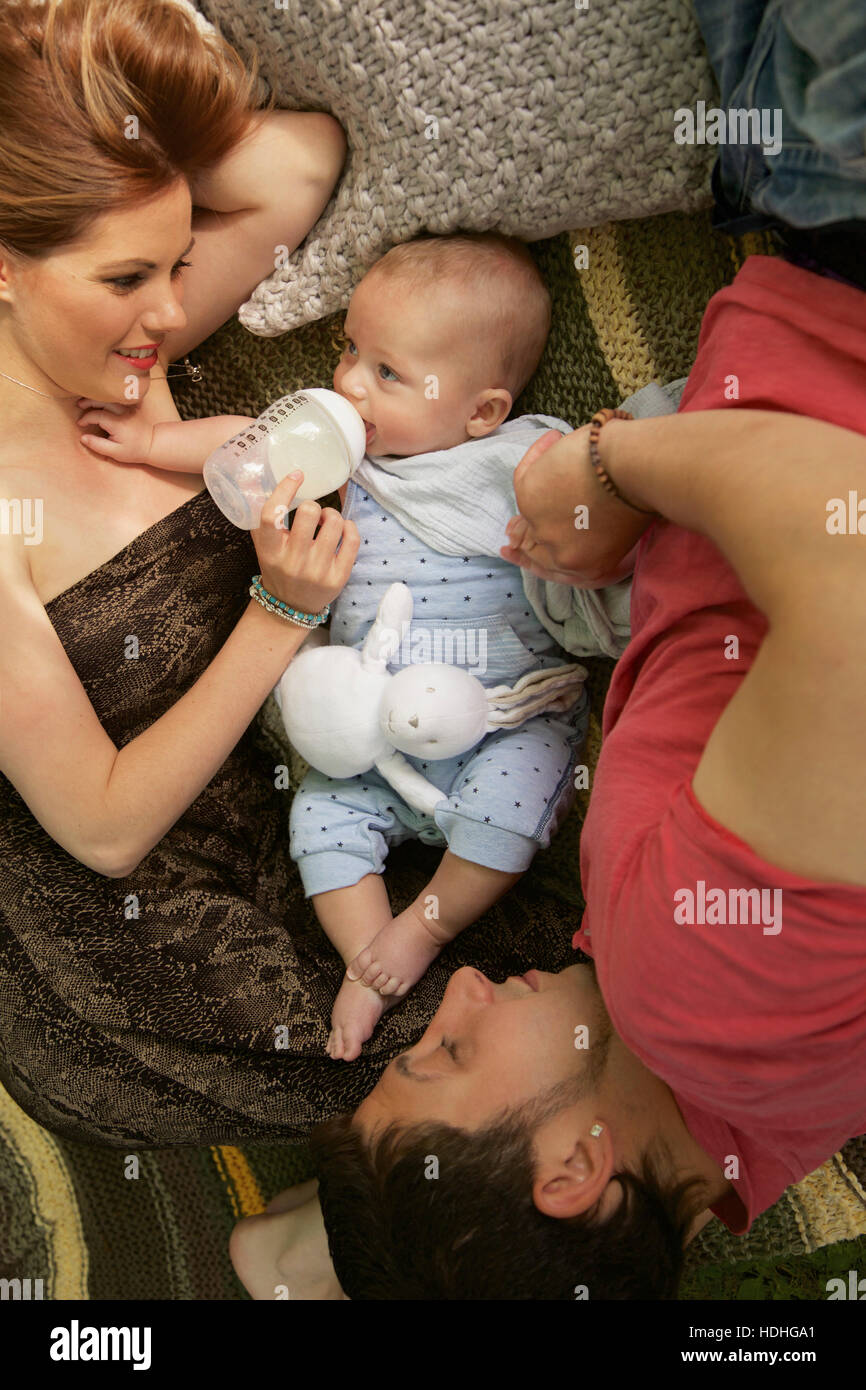 Directly above shot of woman feeding baby boy with bottle while man lying on bed at home Stock Photo