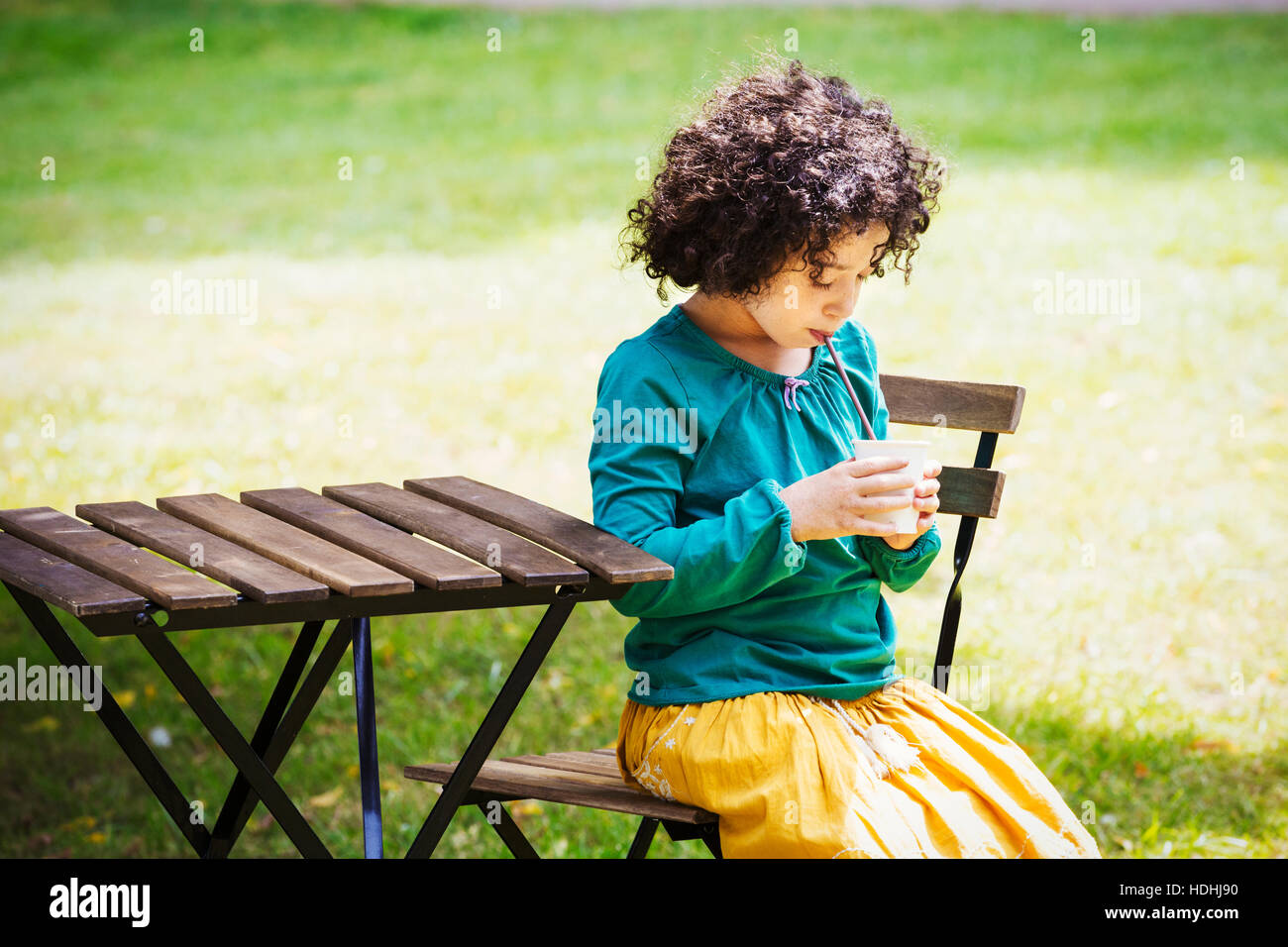 Girl sitting outdoors at a table, having a drink. Stock Photo