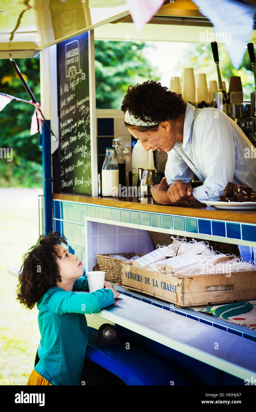 Woman leaning over the counter of a mobile coffee shop, talking to girl. Stock Photo