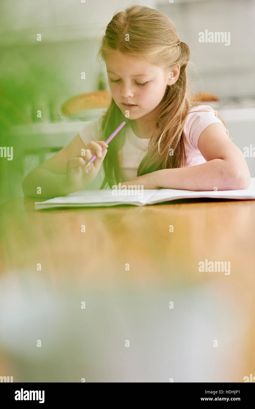 A girl seated at a table with a pencil, doing her homework. Stock Photo