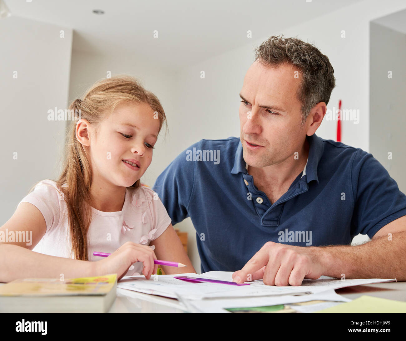 A young girl and her father sitting looking at her school books, doing her homework. Stock Photo