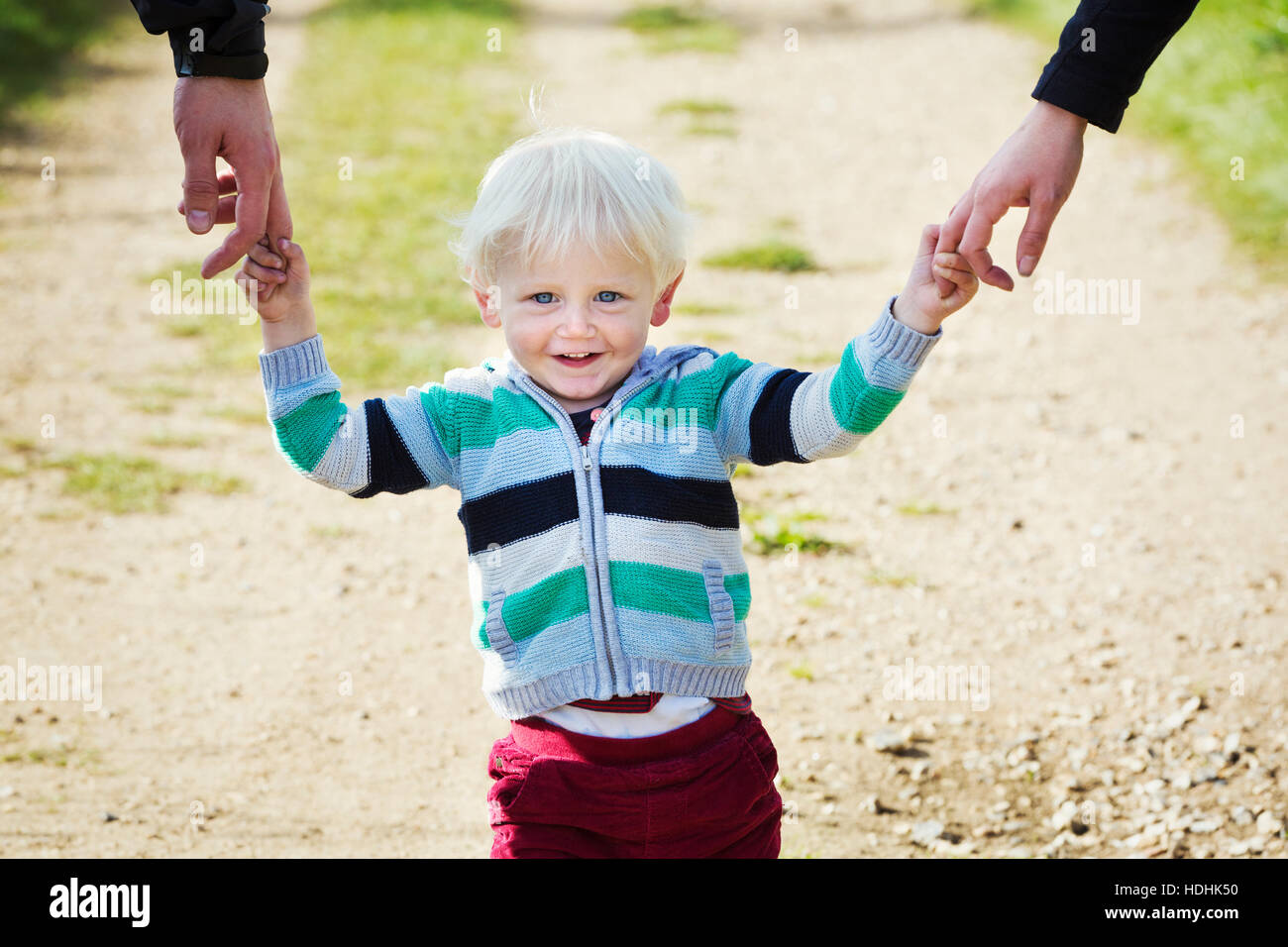 A young boy holding the hands of two adults on a rural path. Stock Photo