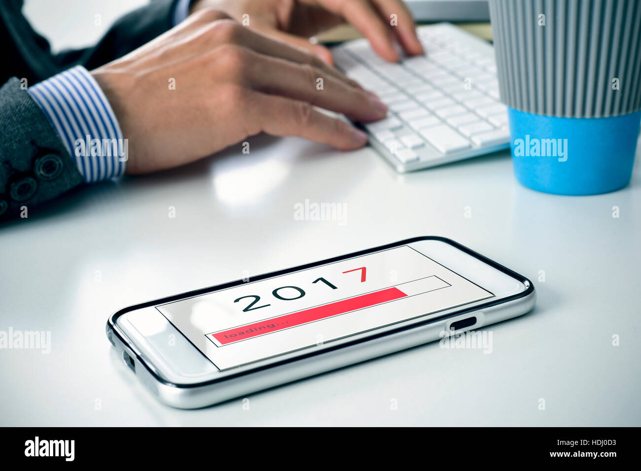 closeup of a young caucasian man sitting at his office desk where there is a smartphone with the number 2017, as the new year, loading in its screen Stock Photo