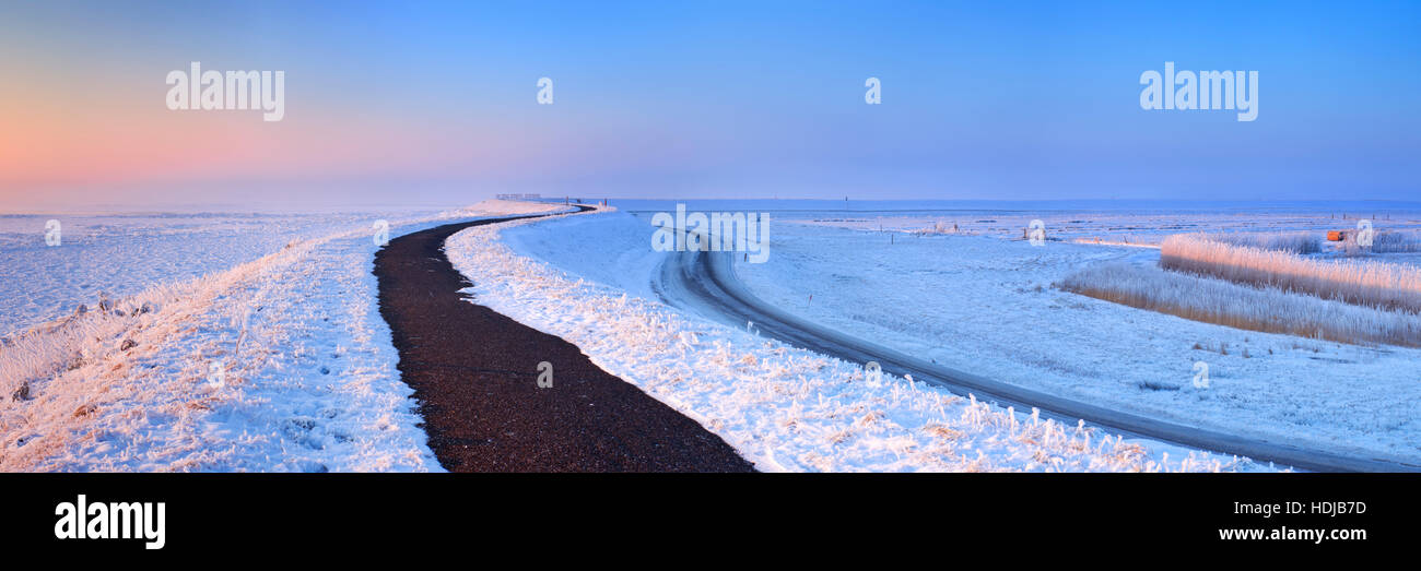 Sunrise over a dike along a frozen lake on a record-breaking cold morning near Uitdam in The Netherlands. Stock Photo