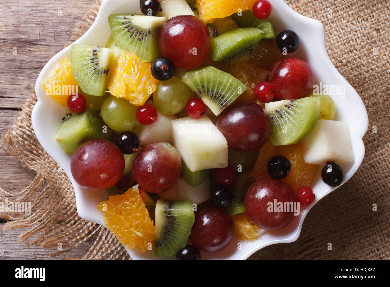 Fruit salad in white plate on the table close-up. horizontal view from above, rustic style Stock Photo