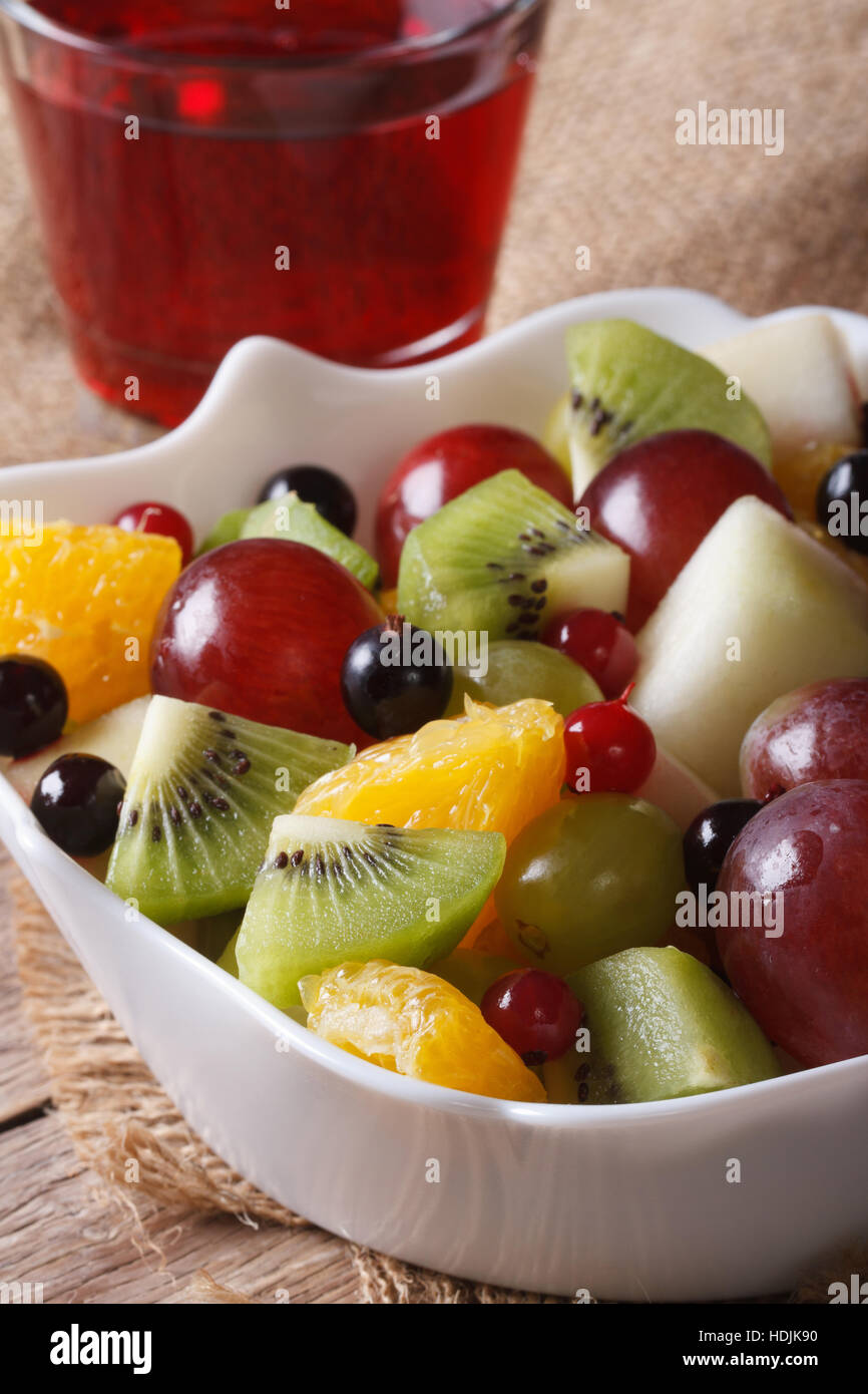 Fruit salad of oranges, grapes. pears, kiwis in a white bowl and grape juice closeup. Vertical Stock Photo