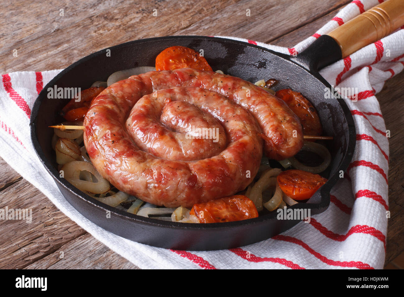 Fried sausage with onions and tomatoes in a pan closeup, rustic style Stock Photo