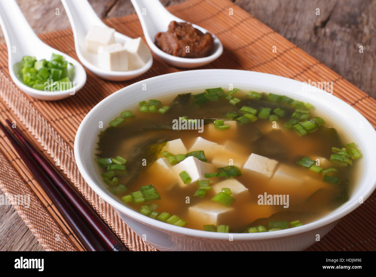 Japanese miso soup in a white bowl and ingredients in a spoon on a table close-up. horizontal Stock Photo