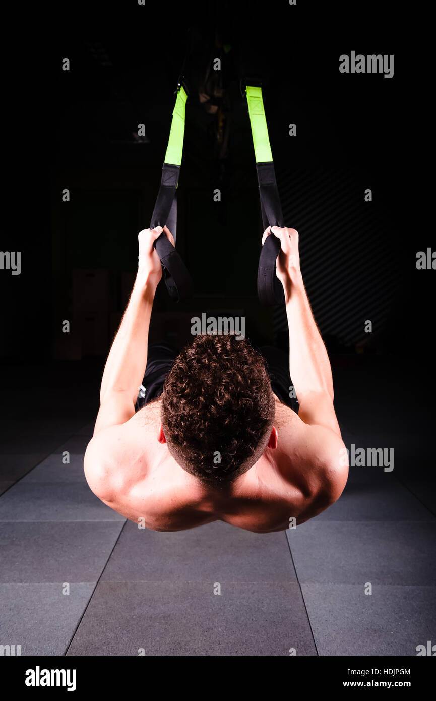 One young handsome brave curly bearded muscled man with a beard makes Total Resistance eXercises fitness trx straps working out in gym Stock Photo